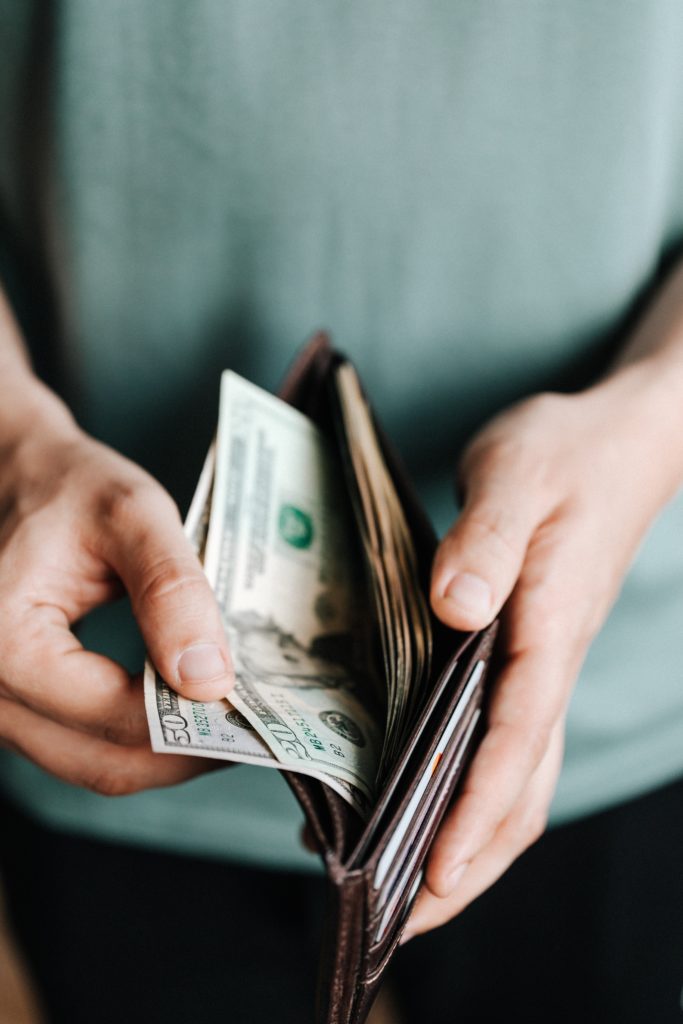 A oerson pulls crisp cash bills out of a brown wallet