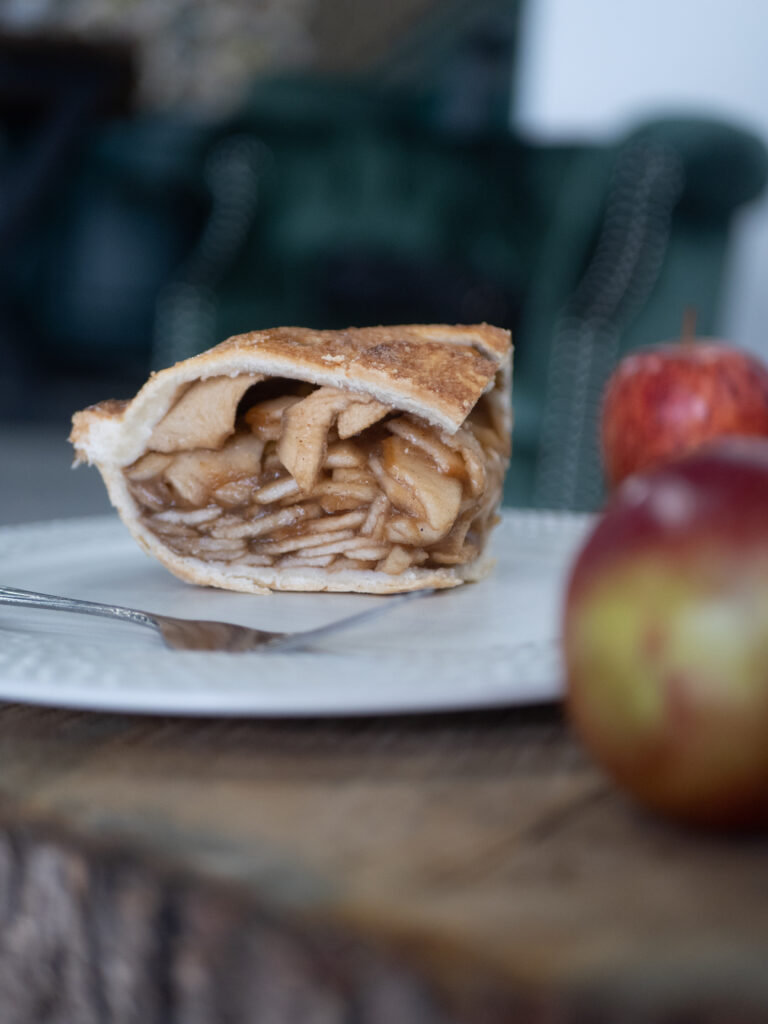 a slice of apple pie on a plate surrounded by apples.