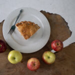 a slice of apple pie on a plate surrounded by apples