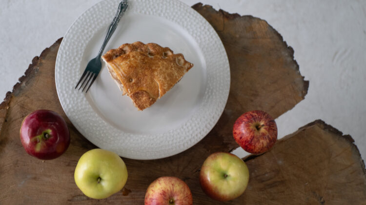 a slice of apple pie on a plate surrounded by apples