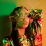 Smoking, activity. Fashionable young woman standing in the studio with neon light.