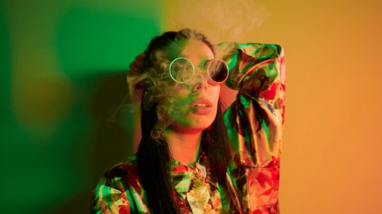 Smoking, activity. Fashionable young woman standing in the studio with neon light.